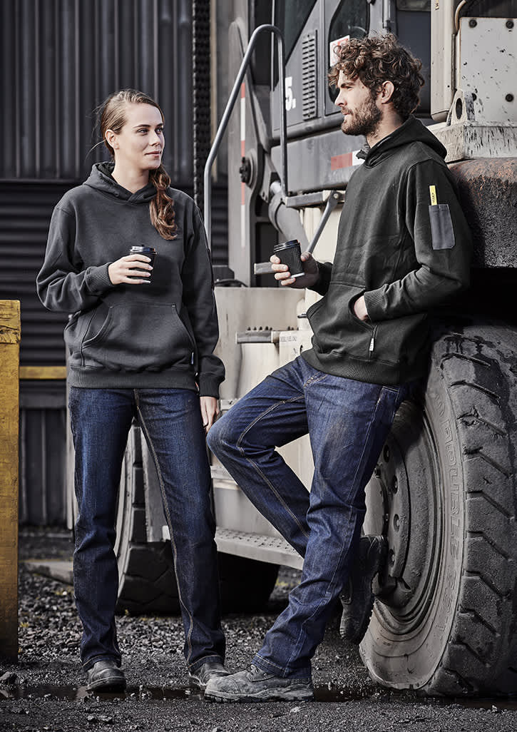 A pair of people wearing black hoodies and blue stretch denim work jeans, standing beside a large vehicle tire. Womens Stretch Denim Work Jean - Image 1