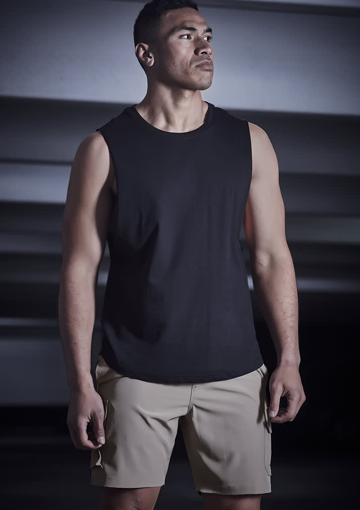 A man wearing a black sleeveless top and beige sports shorts stands in a dimly lit setting. The shorts feature a logo. Mens Streetworx Board Short - Image 1