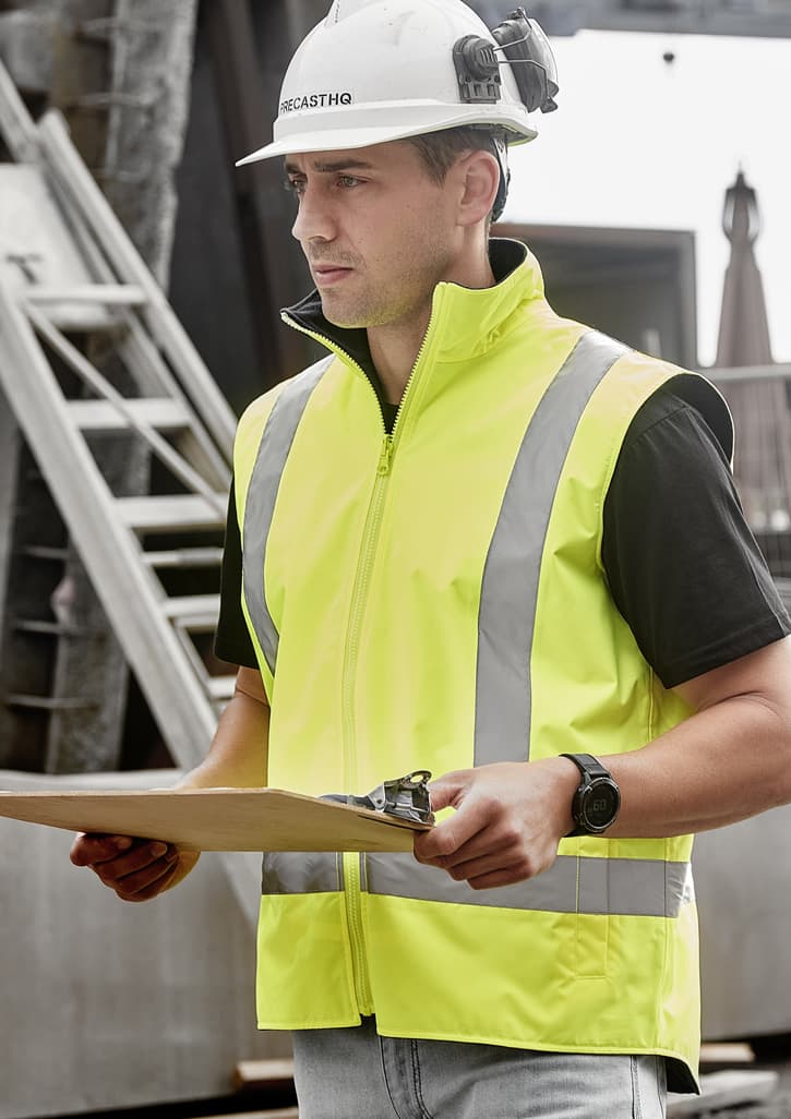 A man wearing a bright yellow waterproof reversible vest with reflective stripes, holding a clipboard. Unisex Hi Vis Waterproof Reversible Vest - Image 1