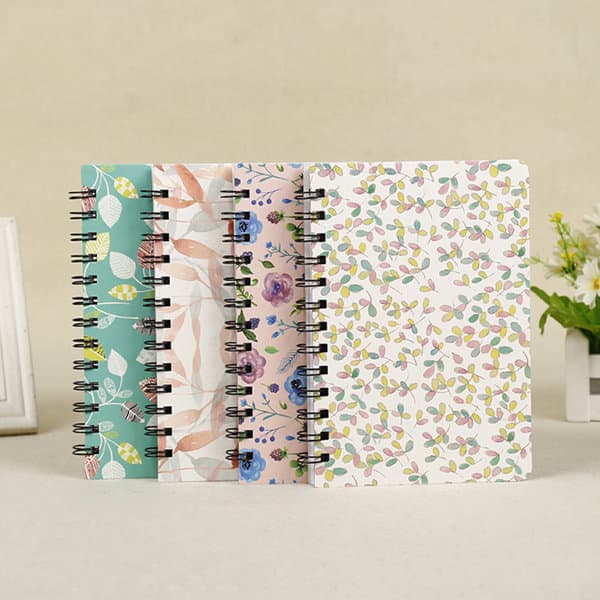 Four spiral-bound hardcover planners in various floral and leaf designs, featuring pastel colours and a logo on the front. B6 Hardcover Planner Spiral Journal - Image 1