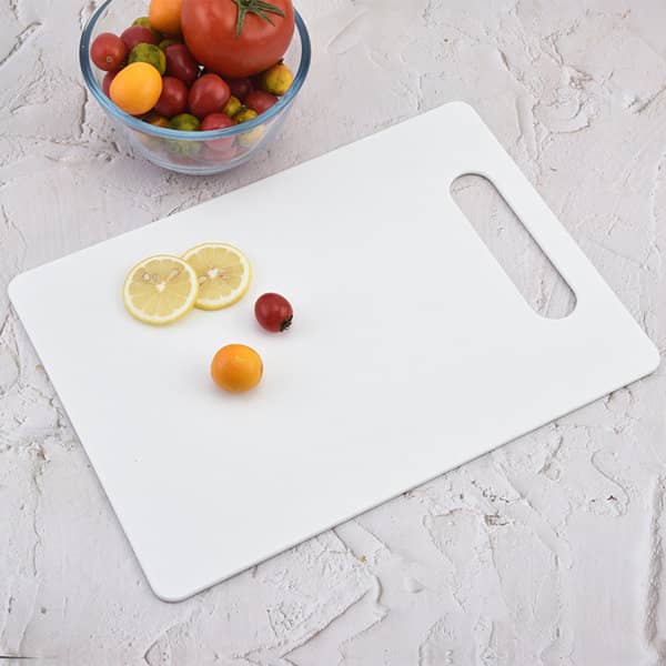 A white plastic cutting board with a grip handle and slices of lemon, beside a bowl of colourful tomatoes. Plastic Cutting Board With Grip - Image 1