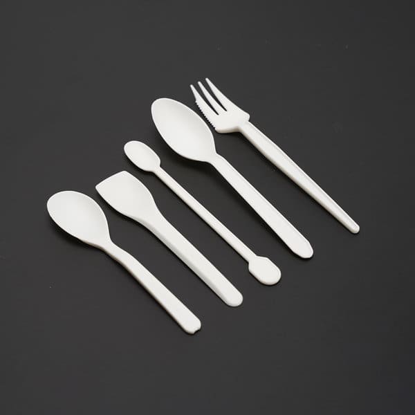 A set of five white PLA degradable dessert forks and spoons arranged on a dark background. 5pcs PLA Degradable Dessert Fork Spoon - Image 1