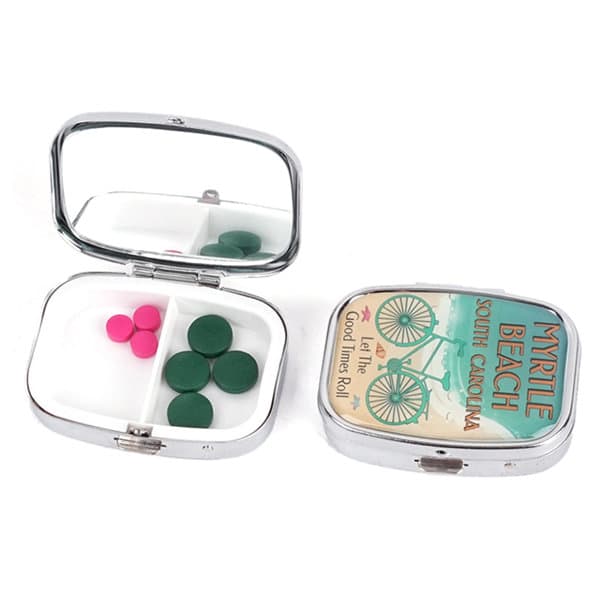 A portable metal pill box with a mirror, featuring green and pink pills, in a shiny silver finish. Portable Metal Pill Box With Mirror - Image 1