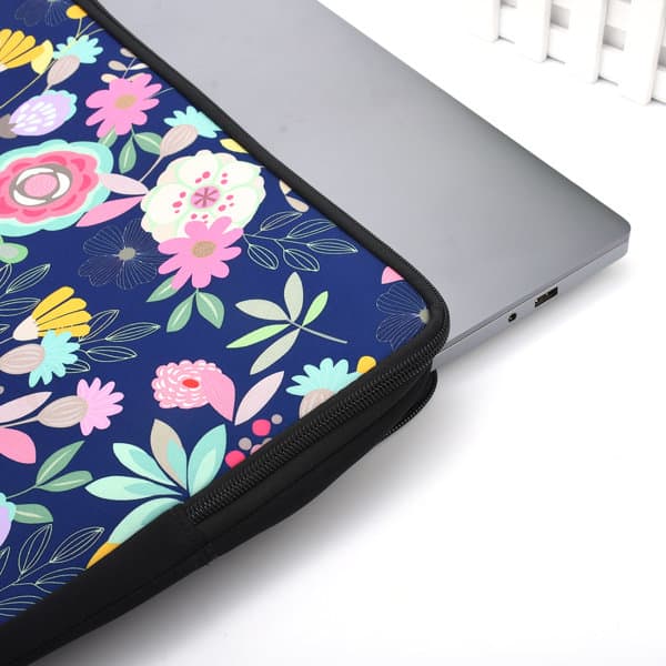 A zippered neoprene laptop sleeve with a floral pattern in vibrant colours, partially covering a silver laptop. Zippered Neoprene Laptop Sleeve - Image 1