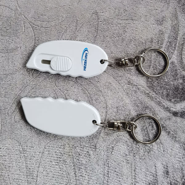 A white mini plastic safety box cutter with a keychain attachment, featuring a smooth design and a metal keyring. Mini Plastic Safety Box Cutter With Keychain - Image 1