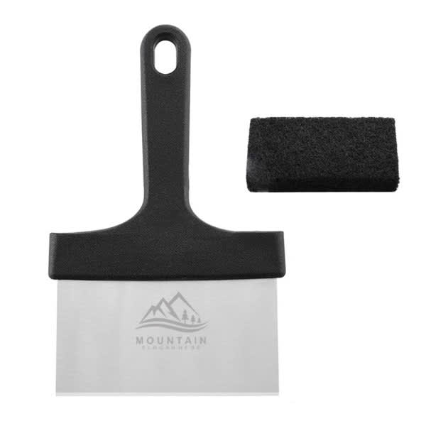 A stainless steel griddle scraper with a black handle and a cleaning pad is displayed. It features a logo. Stainless Steel Griddle Scraper With Black Handle - Image 1