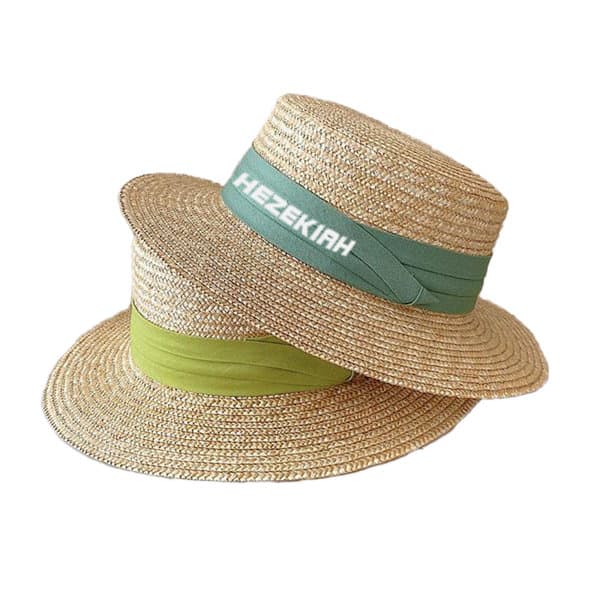 A pair of wheat straw sun hats featuring green and light green bands, each with a branding logo. Wheat Straw Sun Hat - Image 1