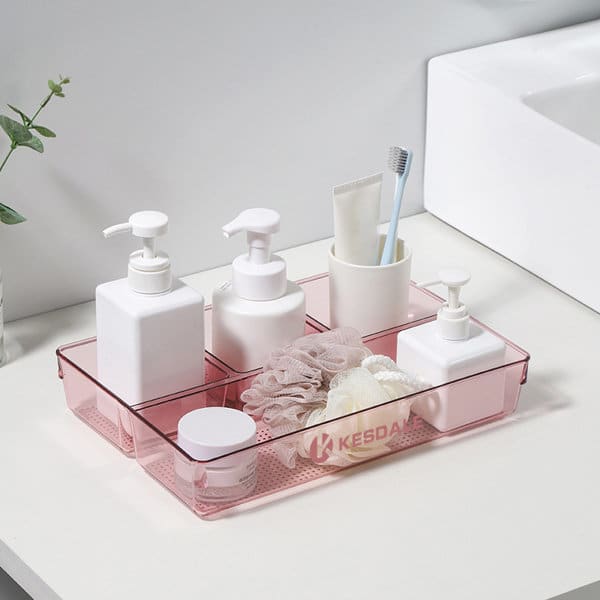 A pink compartment cosmetic tray featuring various white containers and accessories, set on a bathroom countertop. Compartment Cosmetic Tray - Image 1
