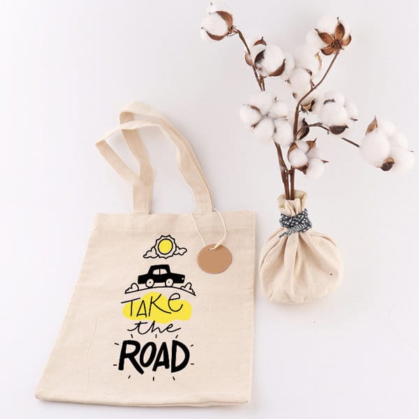 A natural canvas tote bag with a design featuring a car, cloud, and sun, alongside a vase of cotton stems. Custom RPET Reusable Tote Bag - Image 1