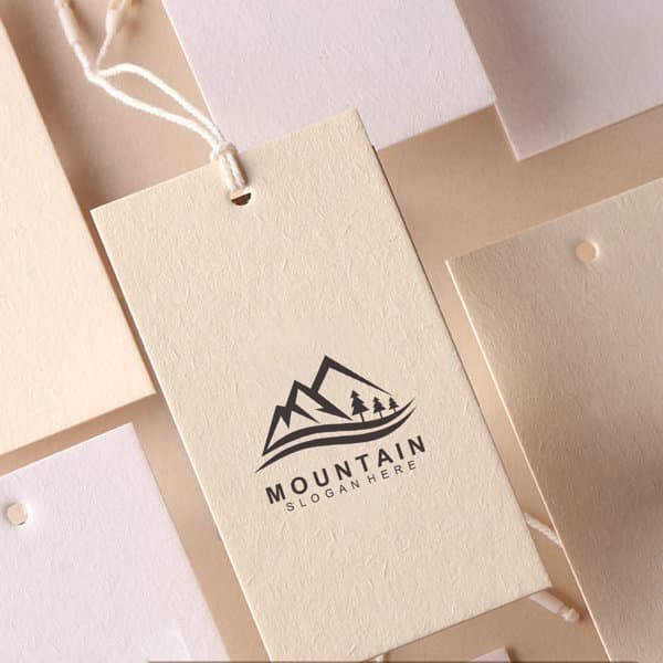 A custom cotton clothing hang tag in cream with a mountain logo. Features a string for attachment. Custom Cotton Clothing Hang Tag - Image 1