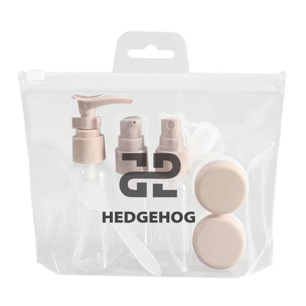 A clear toiletry bag containing four small, beige travel bottles and two containers. The bag features a logo. Clear Travel Bottles Set - Image 1