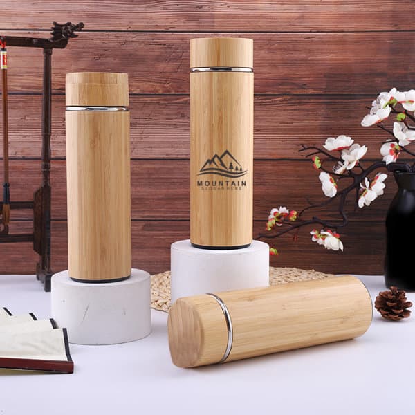 A drink bottle made of bamboo with a sleek design, featuring a logo and placed on a marble stand. 12 oz. Bamboo Insulated Water Bottle - Image 1