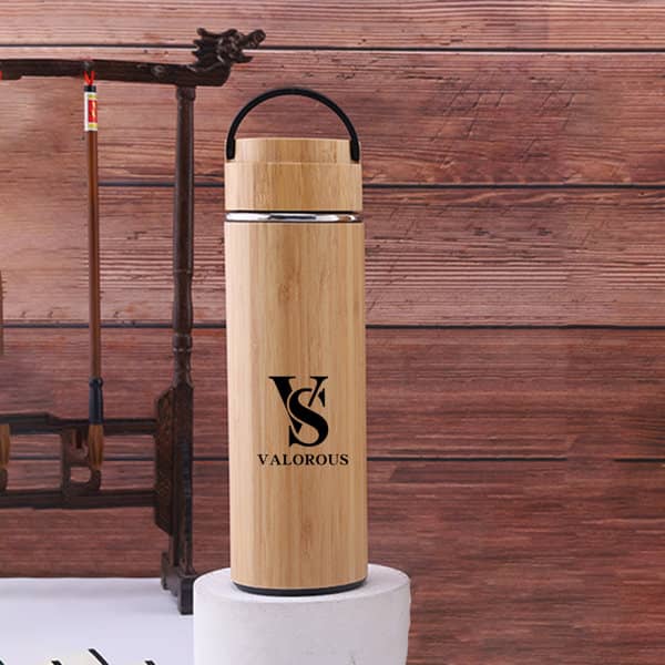 A drink bottle made of bamboo with a handle, featuring a logo, against a rustic wooden backdrop. 15 oz. Bamboo Insulated Water Bottle With Handle - Image 1