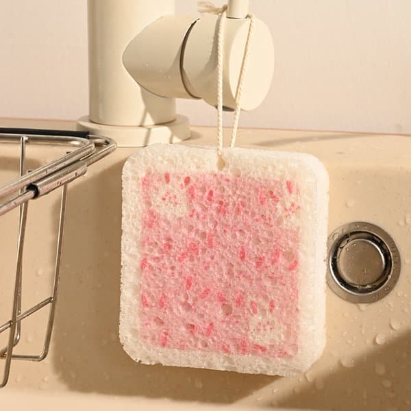 A pink and white sponge hangs near a sink, featuring a textured surface and a hanging loop. Wood Pulp Cotton Cute Magic Sponge - Image 1