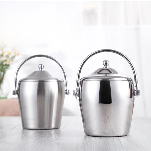 Two stainless steel ice buckets with lids, featuring polished finishes and metal handles, set on a wooden surface. Custom Stainless Steel Ice Bucket With Lid - Image 1