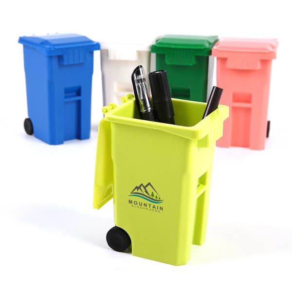 A vibrant green trash can pen holder filled with pens, surrounded by blue, white, pink, and red similar holders. Trash Can Pen Holder - Image 1