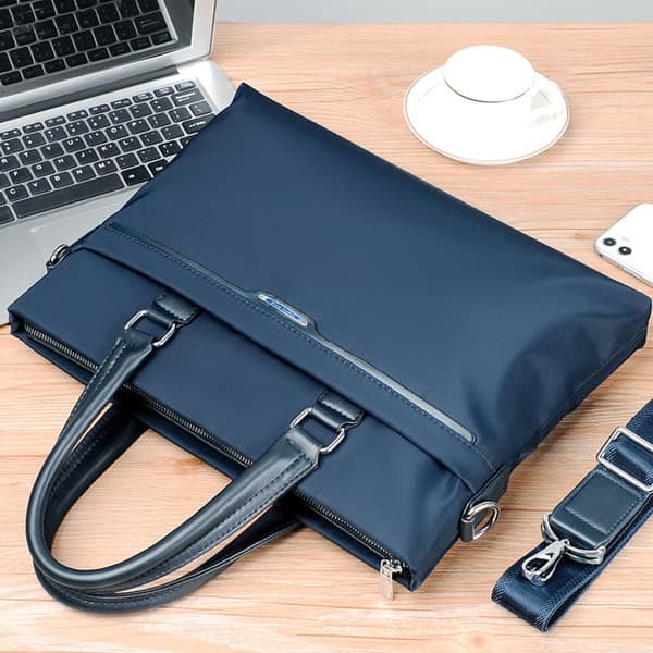 A navy blue business briefcase bag with dual handles and a shoulder strap, placed on a wooden table next to a laptop. Business Briefcase Bag - Image 1