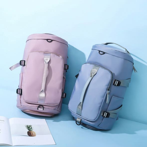 Two gym backpacks in pink and blue, featuring various compartments and straps, alongside an open magazine. Large Gym Backpack With Shoes Compartment - Image 1