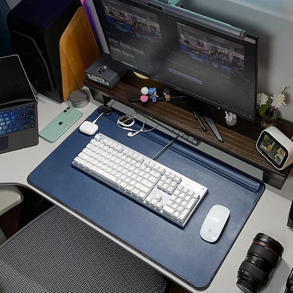 A navy PVC leather desk mat featuring a magnetic cable holder, with a keyboard, mouse, and camera on a desk. PVC Leather Desk Mat With Magnetic Cable Holder - Image 1