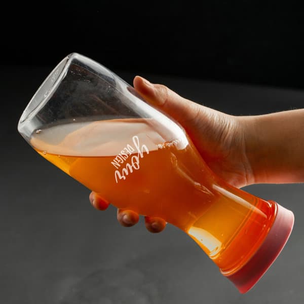 A drink bottle featuring a transparent body, filled with orange liquid, and a red lid. It has a logo on the side. 1L Transparent Juice Water Pitcher With Lid - Image 1