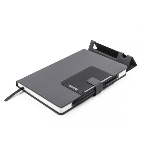 A grey notebook with a mobile phone holder and a black band, featuring a logo on the front cover. Notebook With Mobile Phone Holder - Image 1