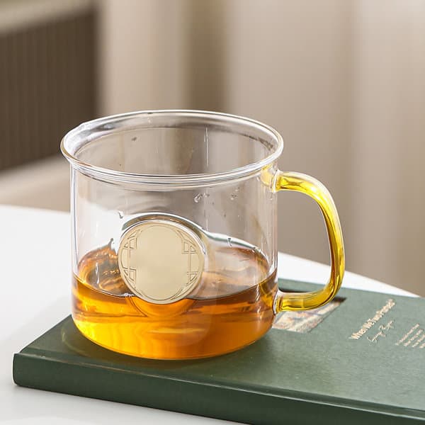 A glass mug featuring a transparent body, yellow handle, and a central engraved medallion, filled with a drink. 18 oz. Custom Engraved Medallion Glass Mug - Image 1