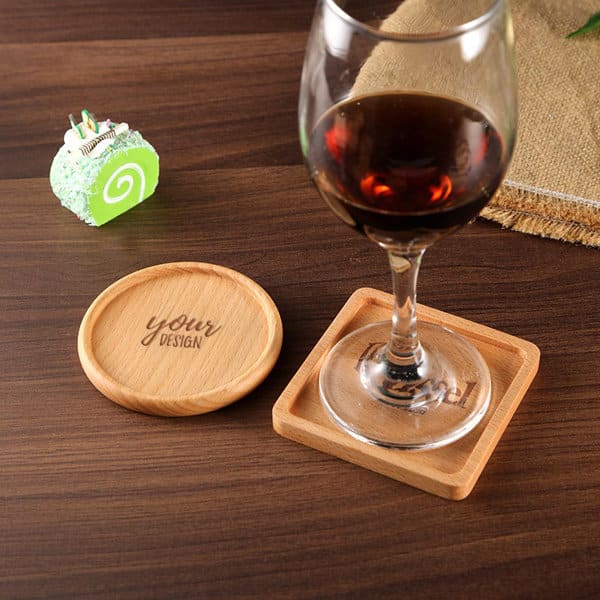 A wooden drink coaster with a square shape beside a round coaster. A wine glass sits on the square coaster. Custom Wood Drink Coaster - Image 1