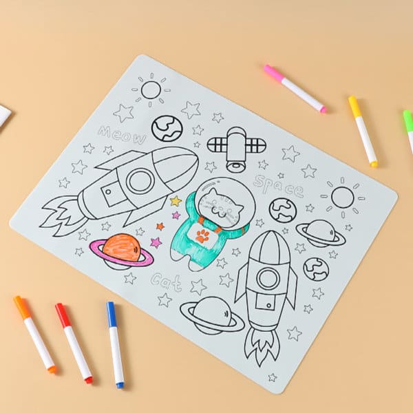 A silicone colouring placemat featuring rockets, planets, and a cat design in grey, with colourful markers around it. Custom Silicone Coloring Placemat - Image 1