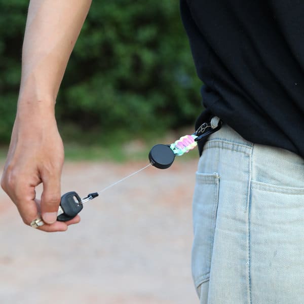 A multitool carabiner retractable keychain in black, attached to a person's belt, with a cord extending from it. Multitool Carabiner Retractable Keychain - Image 1