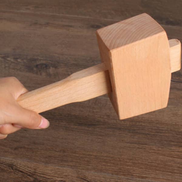 A wooden ice mallet with a light brown handle and square head, held against a wooden surface. Wooden Ice Mallet - Image 1