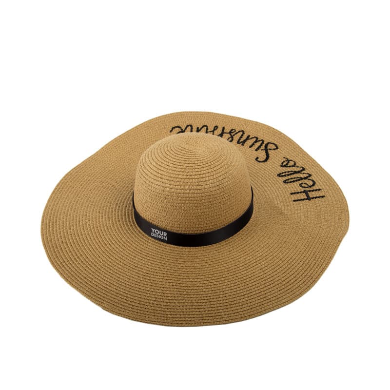 A wide-brim straw hat in tan with a black ribbon band and a logo, featuring a text design. Women Wide Brim Straw Hat - Image 1