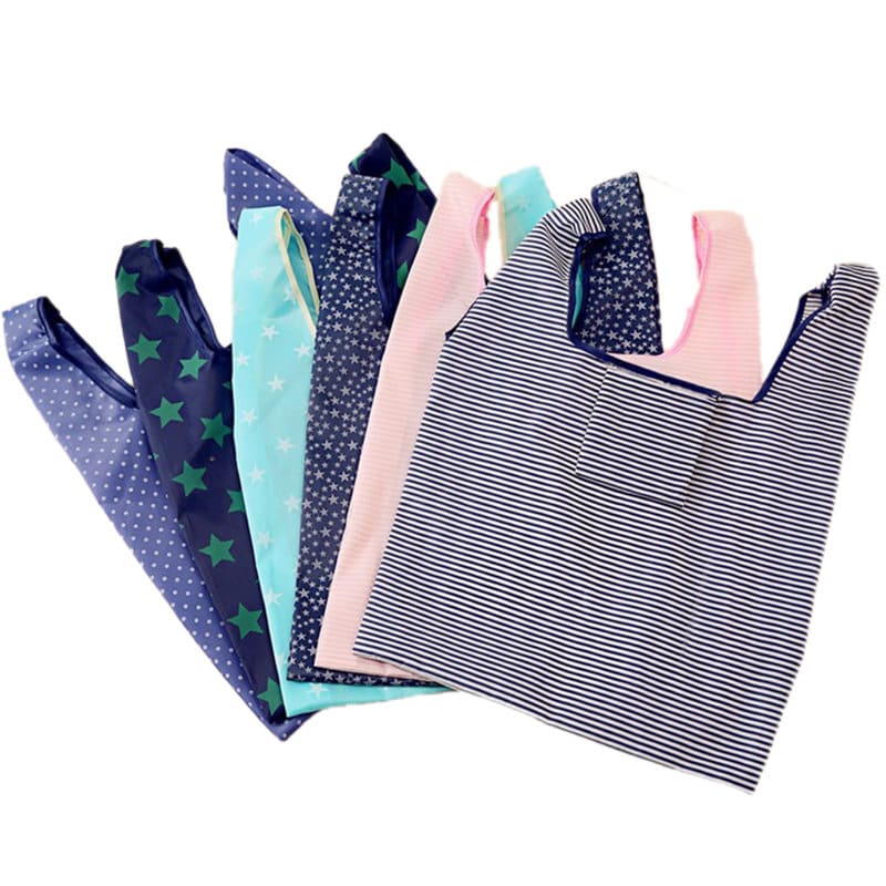 A collection of foldable reusable grocery bags in various colours and patterns, including stripes, stars, and solids. Foldable Reusable Grocery Bag - Image 1