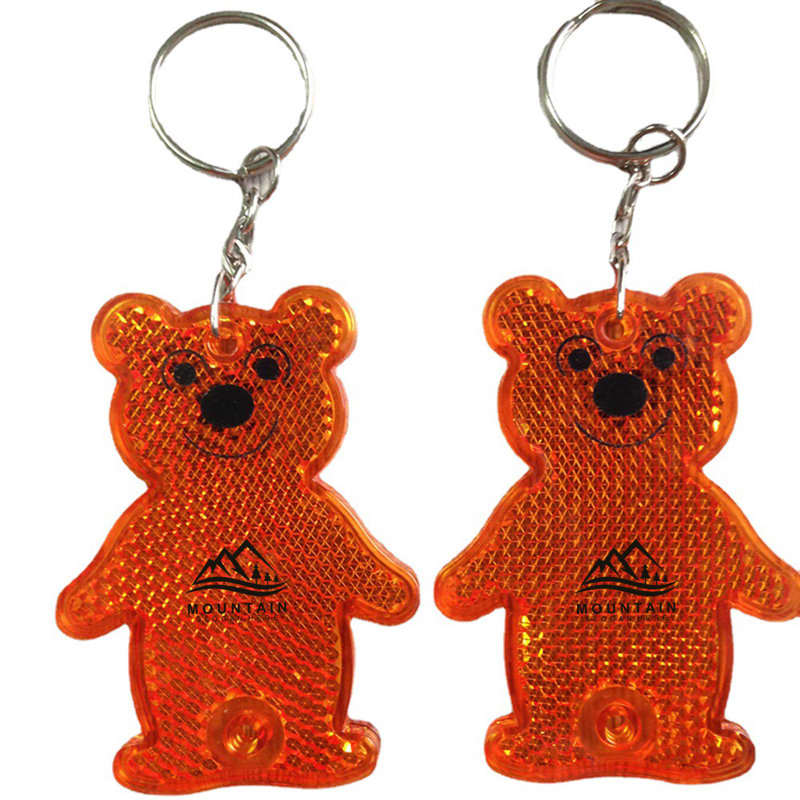 An orange bear-shaped reflective pendant keyring with a silver keyring attachment. It features a simple bear design and a logo. Bear Shape Reflective Pendant Keyring - Image 1