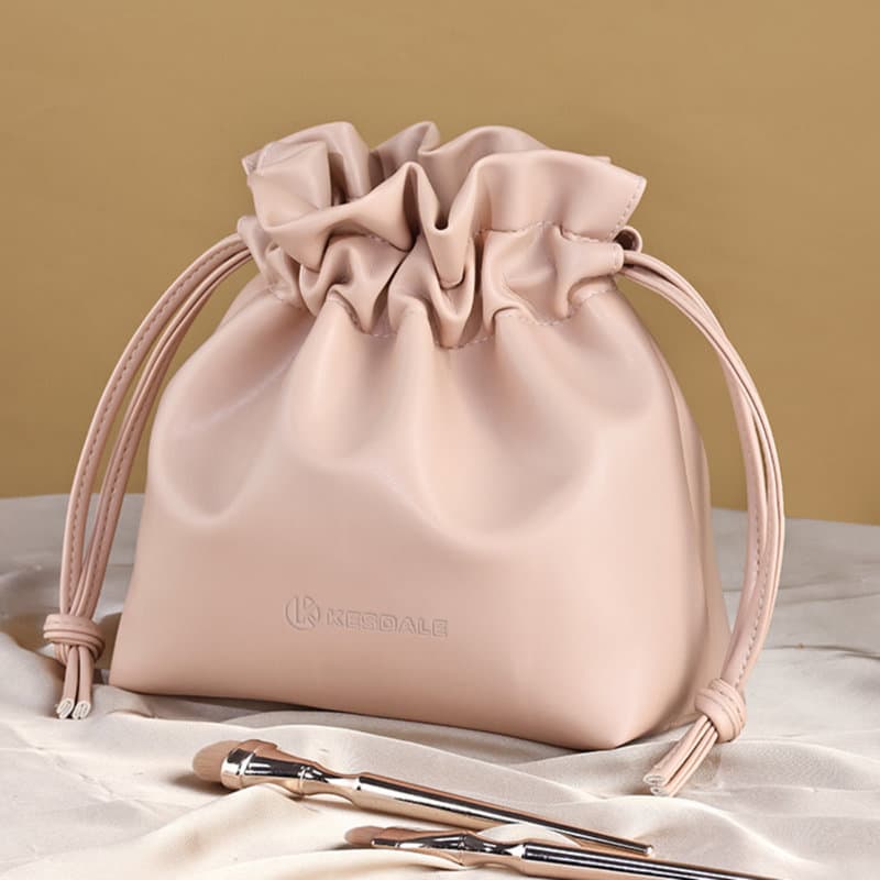 A pink drawstring make-up bag with a ruffled top, accompanied by two make-up brushes. It features a logo design. Drawstring Make Up Bag - Image 1
