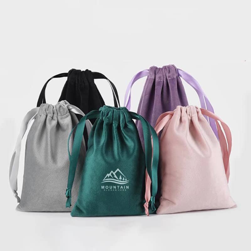 A set of five custom velvet gift bags in grey, green, black, purple, and pink, each with a drawstring closure and a logo. Custom Velvet Gift Bag - Image 1