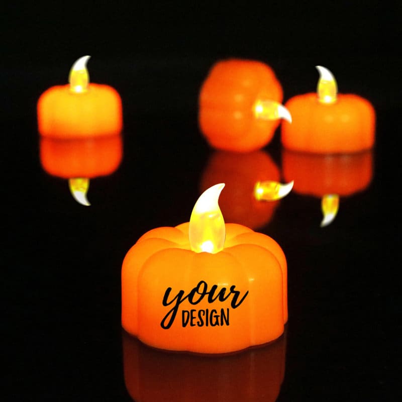 An orange pumpkin-shaped tea light with a flickering flame effect, surrounded by similar lights on a dark surface. Halloween Pumpkin Tea Light - Image 1