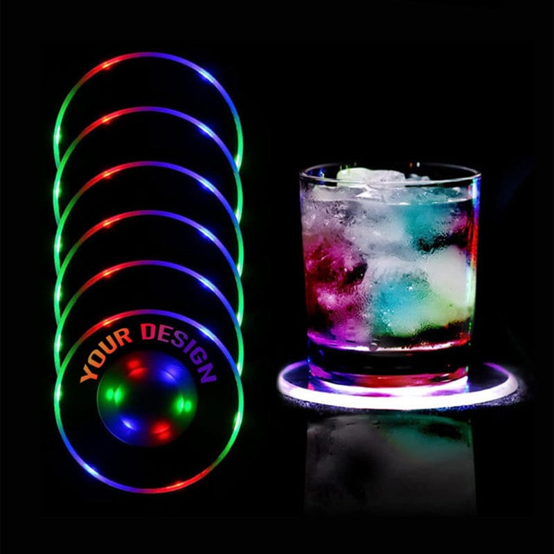 A set of colourful LED coasters in red, green, and blue, beside a glass with ice and a colourful drink. Custom Light Up LED Coasters - Image 1